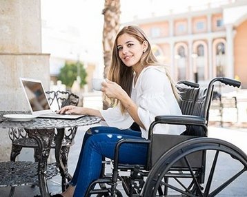 Frau im Rollstuhl mit Notebook an Tisch draußen